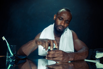 The young african man in bedroom sitting in front of the mirror after scratching his beard at home. Human emotions concept. after shave cream concepts