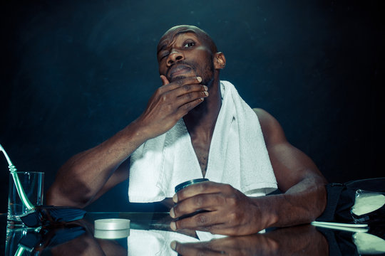 The young african man in bedroom sitting in front of the mirror after scratching his beard at home. Human emotions concept. after shave cream concepts