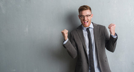 Young redhead elegant business man over grey grunge wall screaming proud and celebrating victory...
