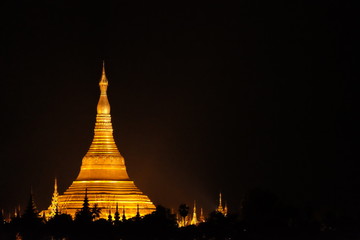 Bright golden Shwedagon pagoda on pure dark clear sky at night surrounded by many smaller pagodas with copy space area