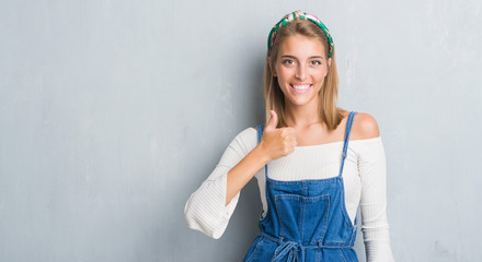 Beautiful young woman standing over grunge grey wall happy with big smile doing ok sign, thumb up with fingers, excellent sign