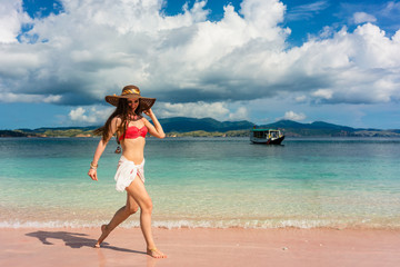 Happy young woman walking through shallow sea water on the beach