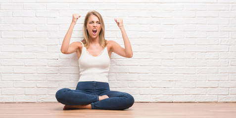 Beautiful young woman sitting on the floor at home angry and mad raising fist frustrated and furious while shouting with anger. Rage and aggressive concept.