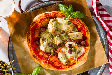 Classic Italian Pizza Margherita with artichokes, olives and capers on a table with beer and a knife. Banner for restaurants, advertising.
