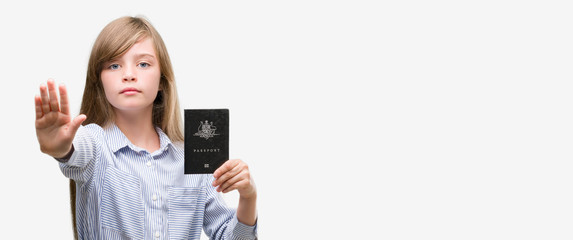 Young blonde toddler holding australian passport with open hand doing stop sign with serious and confident expression, defense gesture