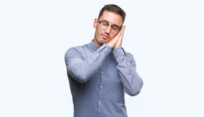 Handsome young elegant man wearing glasses sleeping tired dreaming and posing with hands together while smiling with closed eyes.