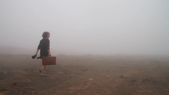 Woman with vintage travel suitcase walks through a cloudy volcanic environment trying to find her way out