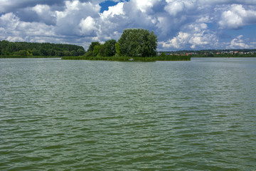 A beautiful image of landscape from the center of the river, surrounded by trees and reeds on the shore and distant horizon against the blue sky in clouds. Reflection, water, tourist destination