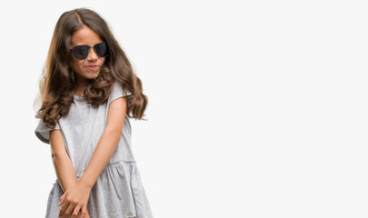 Fototapeta premium Brunette hispanic girl wearing sunglasses looking away to side with smile on face, natural expression. Laughing confident.