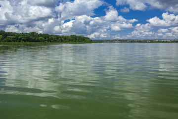 A beautiful image of landscape from the center of the river, surrounded by trees and reeds on the shore and distant horizon against the blue sky in clouds. Reflection, water, tourist destination