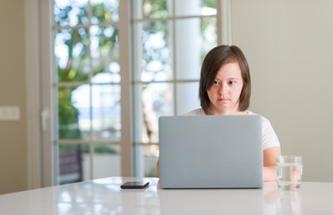 Down syndrome woman at home using computer laptop with a confident expression on smart face thinking serious