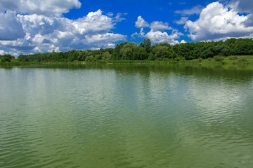 A beautiful image of landscape from the center of the river, surrounded by trees and reeds on the shore and distant horizon against the blue sky in clouds. Reflection, water, tourist destination