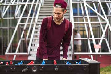 one young man in casual clothes playing foosball in the public park. table games concept