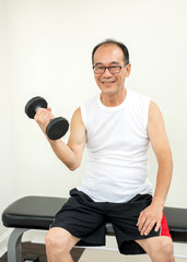 Fototapeta na wymiar Happy Elder Man Lifting Drumbells in Gym with Smile and Happy Emotion - Healthcare and Lifestyle Concept