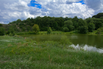 Fototapeta premium A beautiful image of landscape from the center of the river, surrounded by trees and reeds on the shore and distant horizon against the blue sky in clouds. Reflection, water, tourist destination