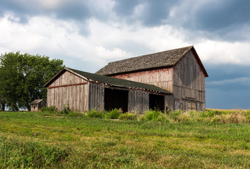 Fototapeta na wymiar Abandoned farm with old painted red barns standing empty on a hill with dark clouds. Gives the feeling of trouble, a storm brewing for farmers. Concepts of family farm, trade wars, tariffs