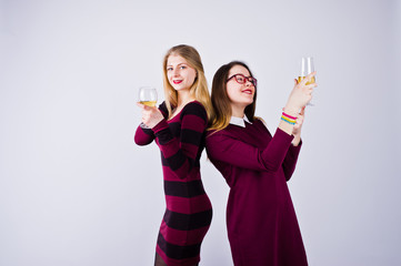 Two attractive friends in purple dresses drink sparkling wine or champagne in the studio.