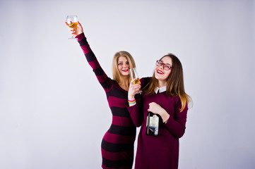 Two attractive friends in purple dresses drink sparkling wine or champagne in the studio.