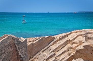 Coastal rock landscape and small boats in turquoise sea with horizon on a sunny summer day in Mallorca, Spain.