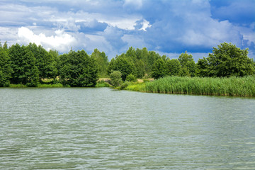 Fototapeta premium A beautiful image of landscape from the center of the river, surrounded by trees and reeds on the shore and distant horizon against the blue sky in clouds. Reflection, water, tourist destination