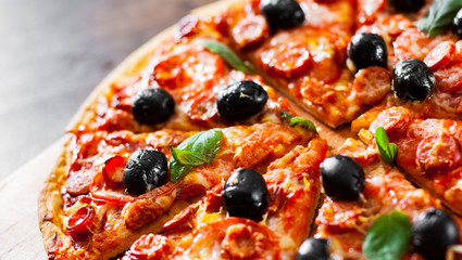 slices of Pizza with Mozzarella cheese, salami, pepper, pepperoni, Tomatoes, olives, Spices and Fresh Basil. Italian pizza on wooden background