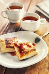 Breakfast with freshly prepared pancakes with strawberry jam and a cup of tea. It is served in a white dish on a wooden table.
