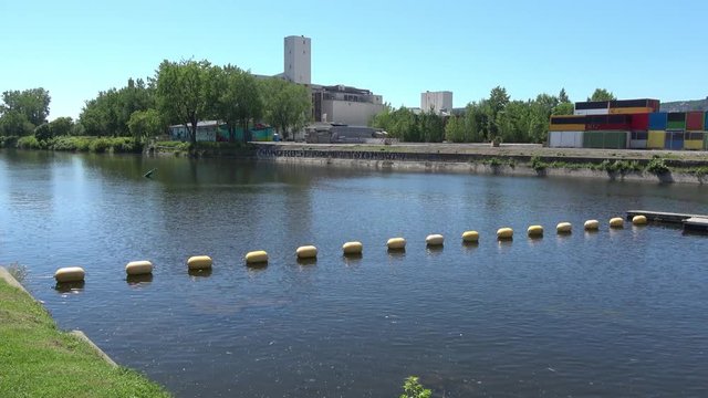 Buoys floating on water in Montreal Lachine canal. City skyline in background. Wide view. Camera pan.
