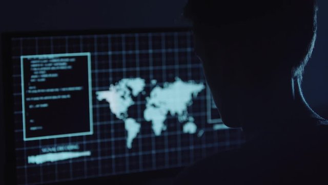 Young Hacker doing Attack on Data Servers and bank's account to still the secret credit card numbers. Working in sci-fi Dark Hideout in front of big screen with fantastic UI interface. Web tehcnology