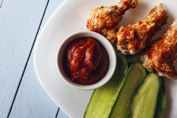 Baked poultry meat, tomato paste and sliced cucumbers on a white plate on a wooden table. Top view from above. Copy space for text