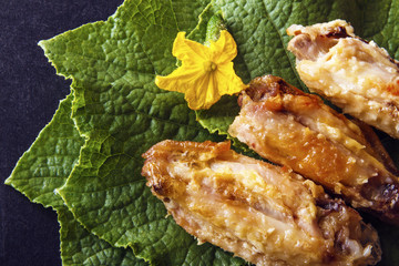 Baked crispy poultry chicken wings on green cucumber leaves on a black background. Top view from above. Copy space for text