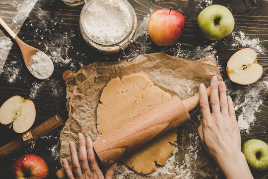 Preparing pie crust for apple pie. Hands rolling dough with rolling pin on the wooden background