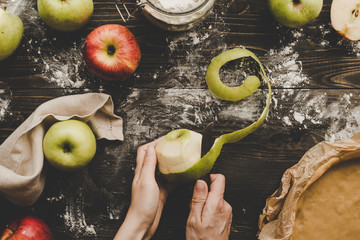 Cooking apple pie. Hands peeling apples for apple pie on the wooden table. Top view
