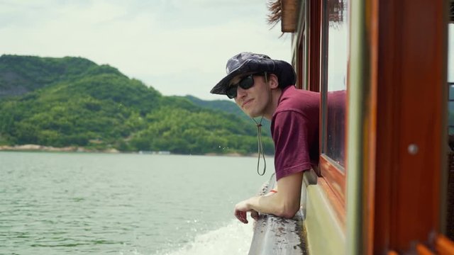 Young male traveller on a boat ponders into the distance. Soaks in the beautiful environment