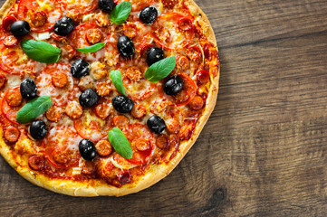 Pizza with Mozzarella cheese, salami, pepper, pepperoni, Tomatoes, olives, Spices and Fresh Basil. Italian pizza on wooden background. with copy space. top view