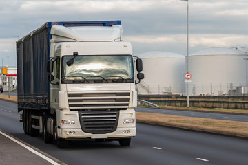 Road transport. Large blue lorry in motion on the road with oil depot in the background