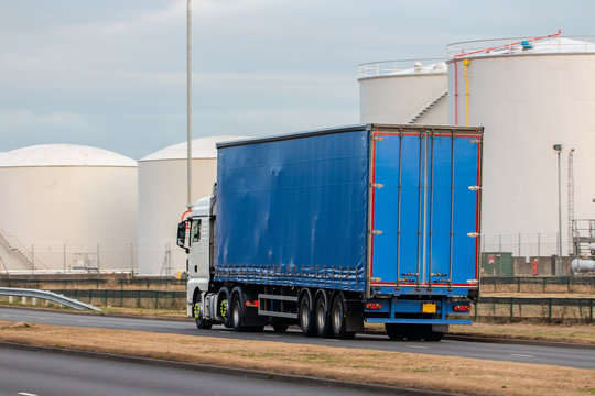Road transport. Large blue lorry in motion on the road with oil depot in the background