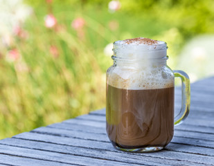 Ice coffee in glass with milk and cinnamon on wooden table in the garden.