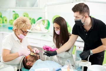 Obraz premium Dentist a woman works with a patient, she is assisted by two assistant: girl and a guy. Modern clinic with new technologies