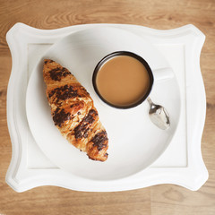 Cup of coffee with croissant on a white plate over white table Breakfast, top view. Square image.