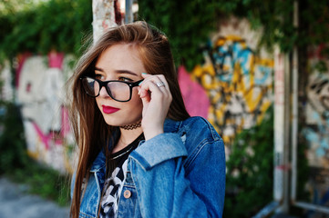 Stylish casual hipster girl in jeans wear and glasses against large graffiti wall.