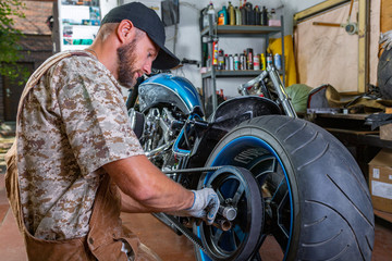 Plakat Side view portrait of man working in garage repairing motorcycle