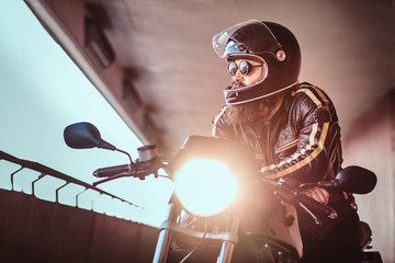 Close-up portrait of a brutal bearded biker in helmet and sunglasses dressed in a black leather...