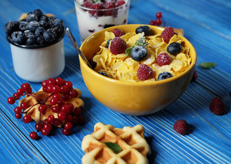 Cornflakes with berries raspberries and blueberries on blue wooden background.