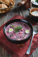Cold beetroot soup in a ceramic plate on a table next to a basket of bread and sour cream
