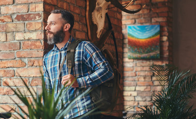 Handsome bearded hipster male in a blue fleece shirt and jeans with backpack leaning against a...