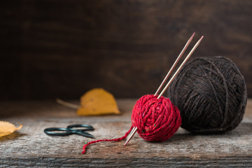Bright red wool yarn with wooden needles among leaves and acorns, autumn knitting postcard