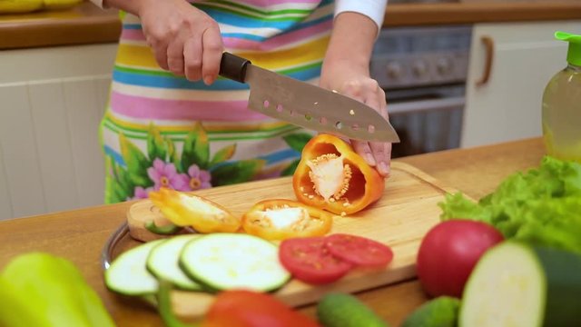 Female hands of housewife with a knife cut fresh bell pepper on chopping Board kitchen table