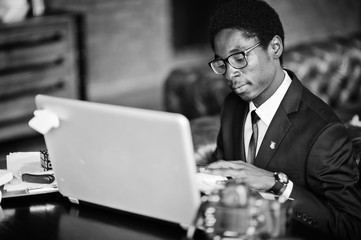 Business african american man wear on black suit and glasses sitting at office with laptop and...