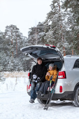 Father and his kid talking together after sports activities such as ski and ice skates. Sitting back trunk of suv at winter season
