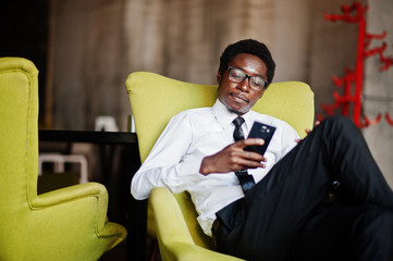 Business african american man wear on white shirt, tie and glasses at office, sitting on chair and looking on phone.